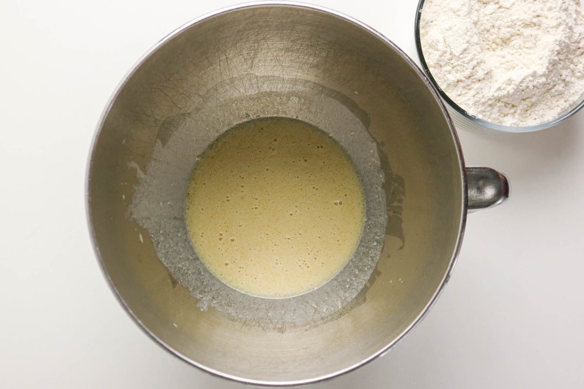 Metal mixing bowl with batter next to a bowl of flour on a white surface.
