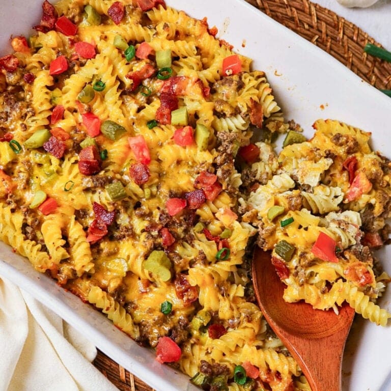 Cheesy pasta bake with ground meat, diced tomatoes, and pickles in a white dish.