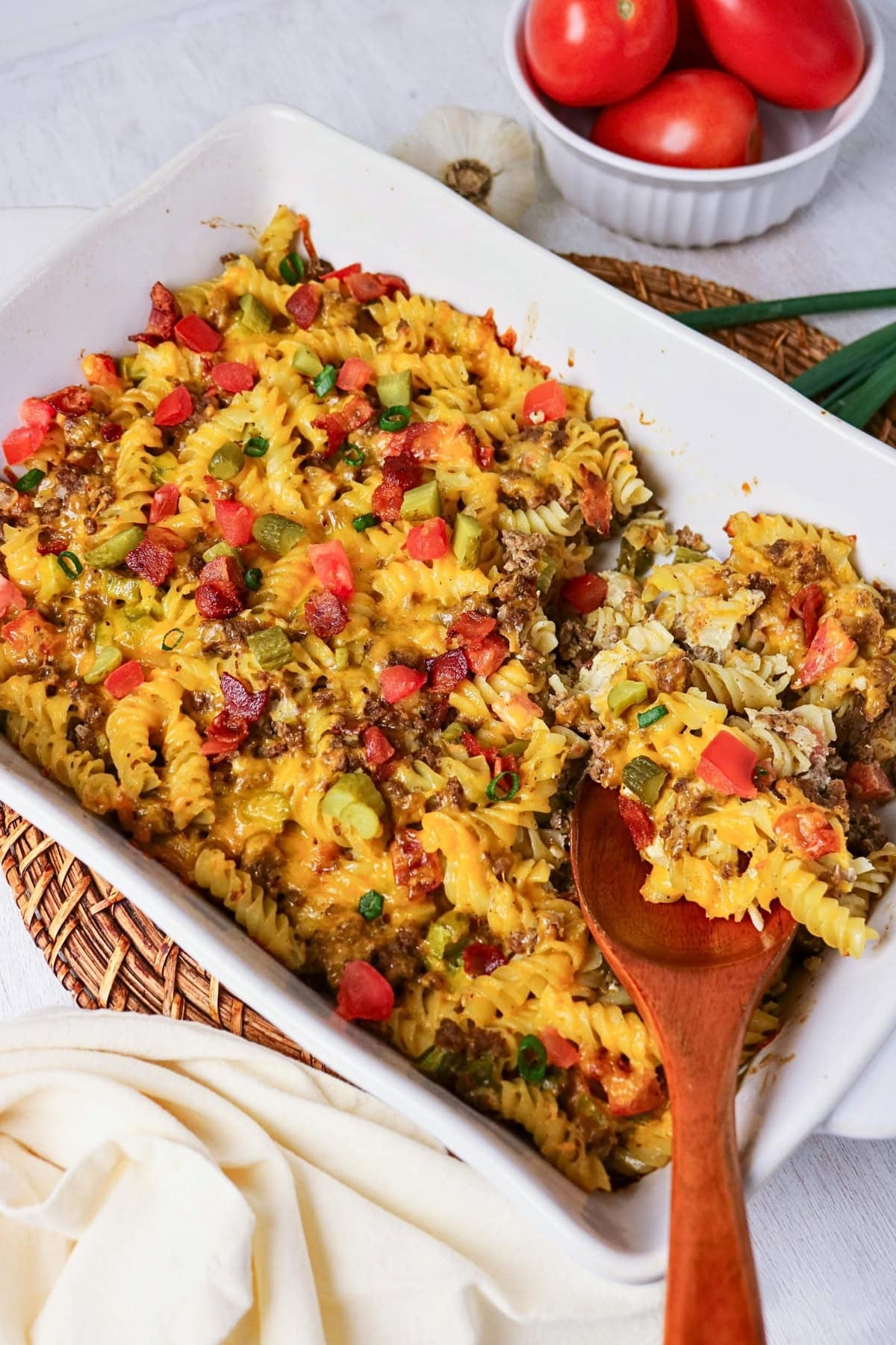 Baked pasta casserole with cheese, tomatoes, green onions, and wooden spoon.