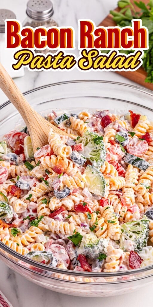 Bowl of bacon ranch pasta salad with a wooden spoon and fresh ingredients.