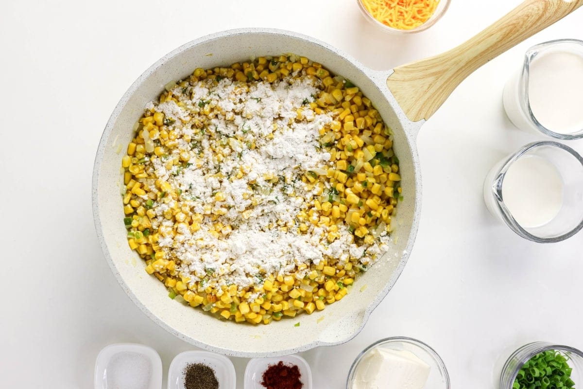 Corn and flour mixture cooking in a skillet, surrounded by bowls of ingredients.