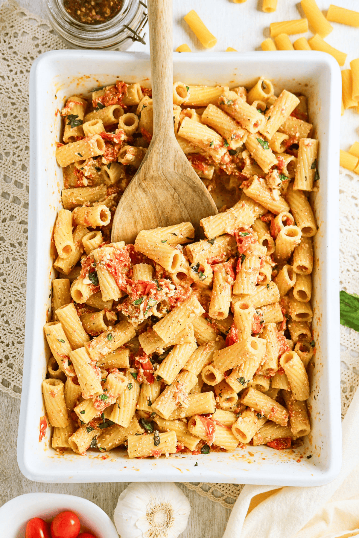 Baked rigatoni pasta with tomatoes, feta, and herbs in a white dish.