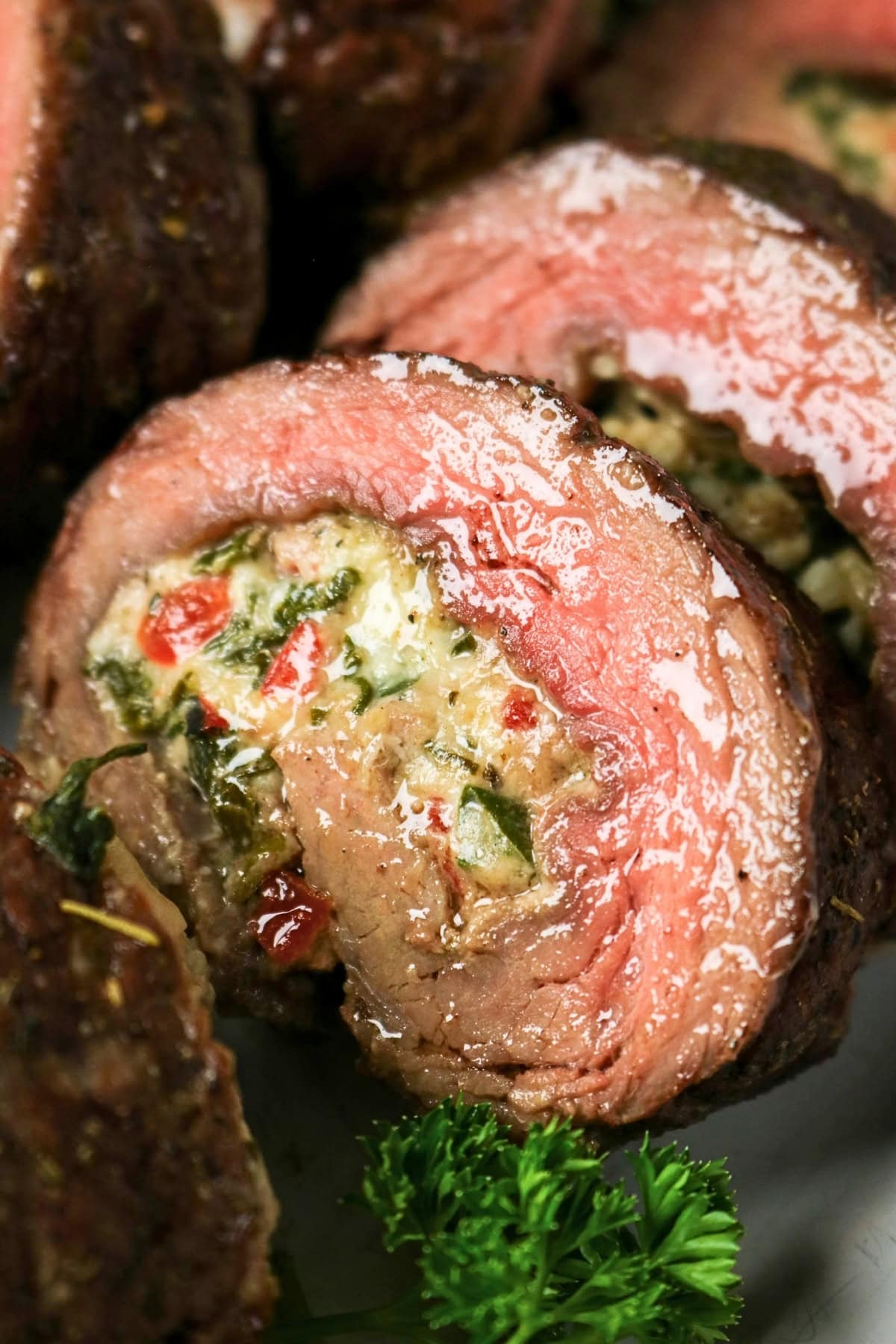 Sliced stuffed steak roll with creamy filling and herbs, garnished with parsley.