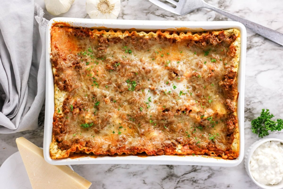 Baked lasagna in a white dish topped with melted cheese and herbs.