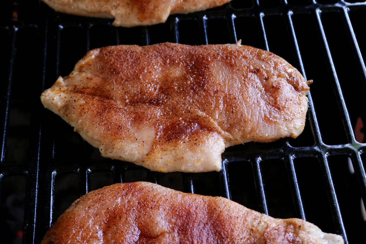 Seasoned chicken breasts cooking on a grill.