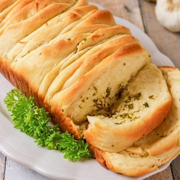 Sliced garlic bread loaf on a white plate with parsley garnish.