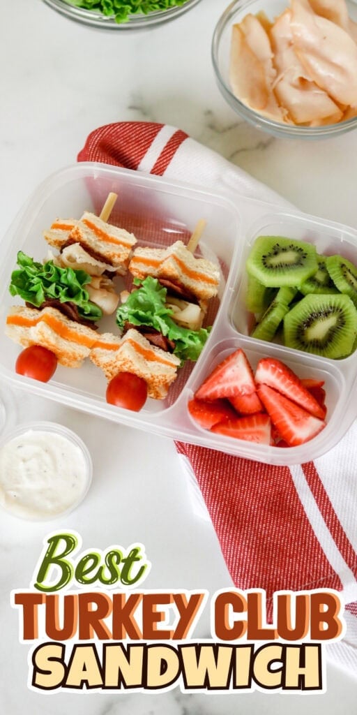 Turkey club sandwich skewers with kiwi, strawberries, and dip in a lunch box.