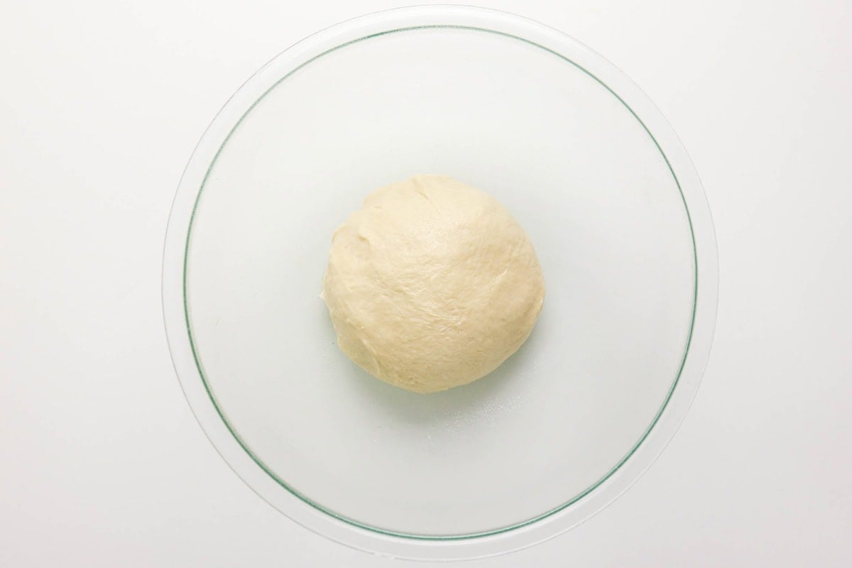 A ball of dough in a clear glass bowl on a white surface.