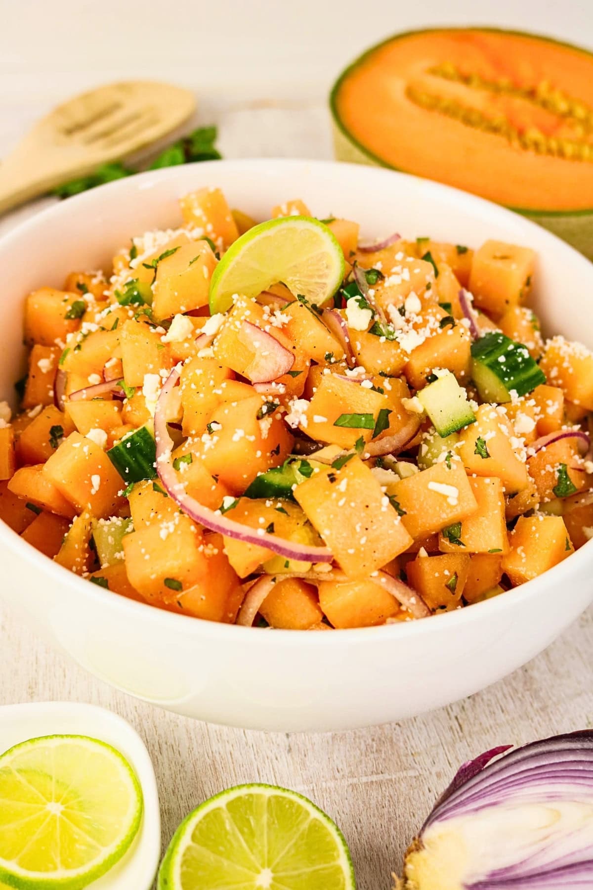 Cubed cantaloupe salad with lime, red onion, cucumber, and cheese in a bowl.