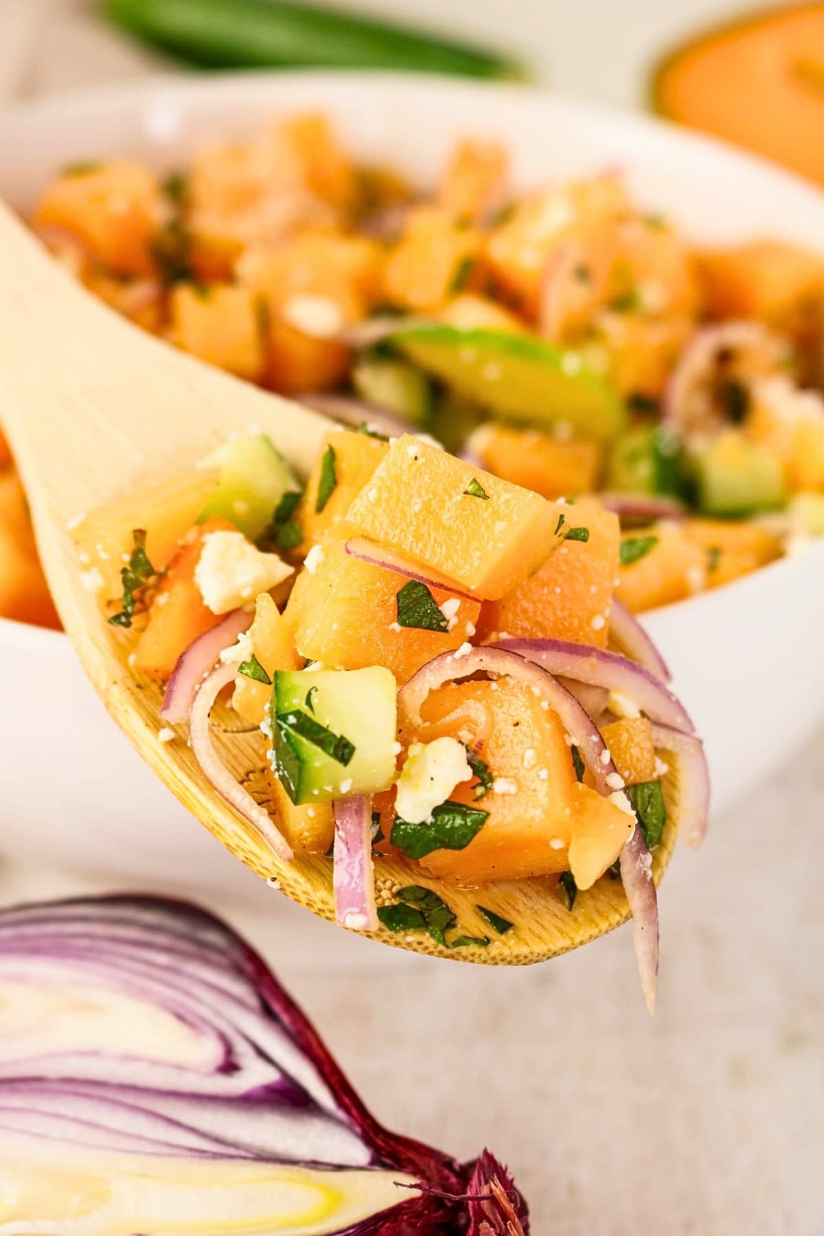 Spoonful of melon salad with onions, cucumber, feta, and herbs.