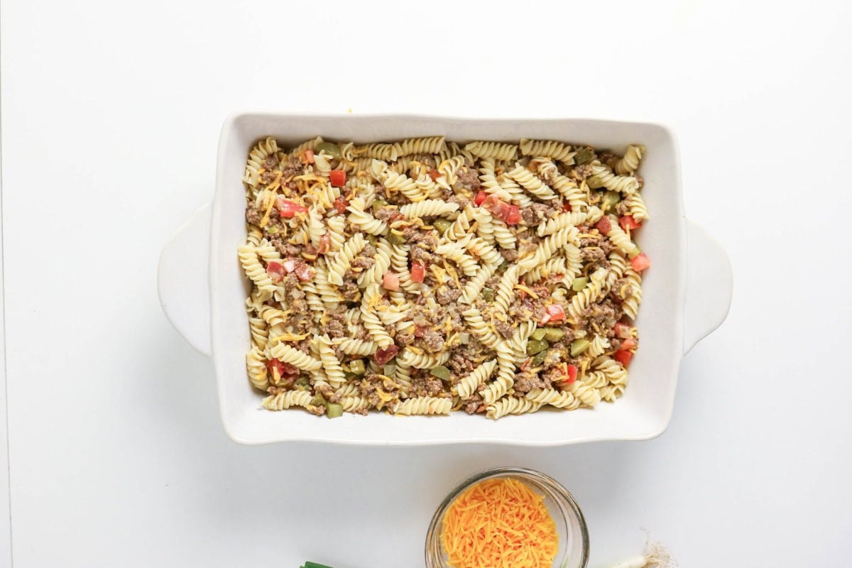 Baking dish with rotini pasta, ground beef, and veggies on white background.