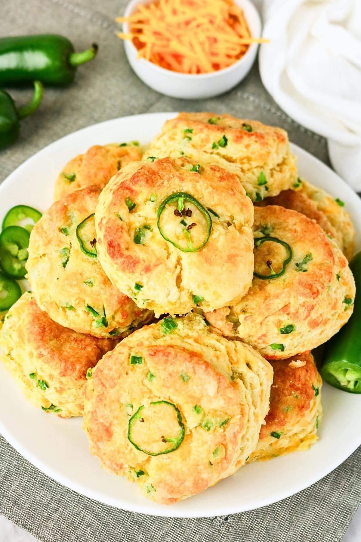 Biscuits topped with jalapeño slices; shredded cheese in the background.