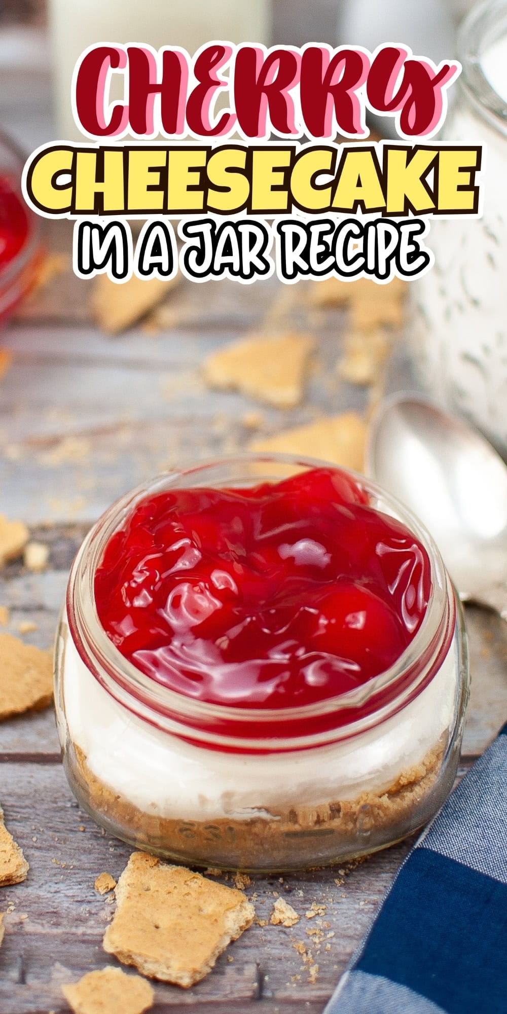A jar of cherry cheesecake sits on a table with graham crackers around it.