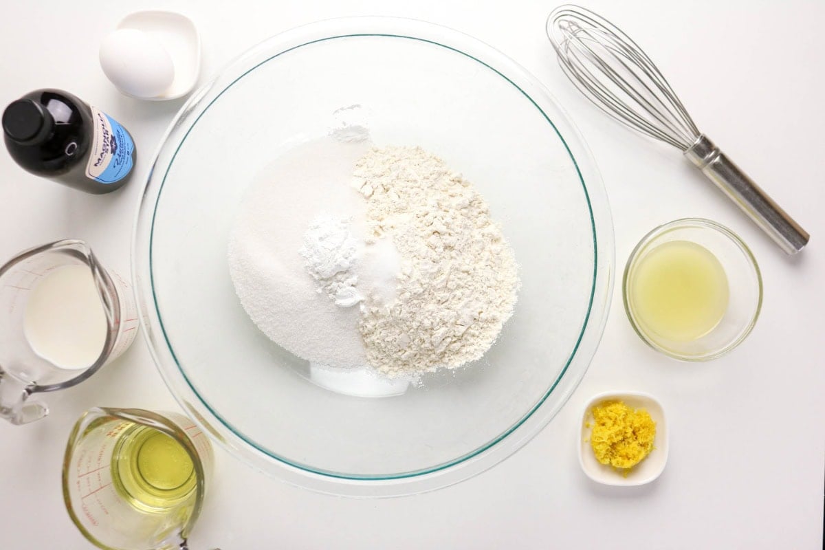Baking ingredients in bowls with a whisk on a white background.