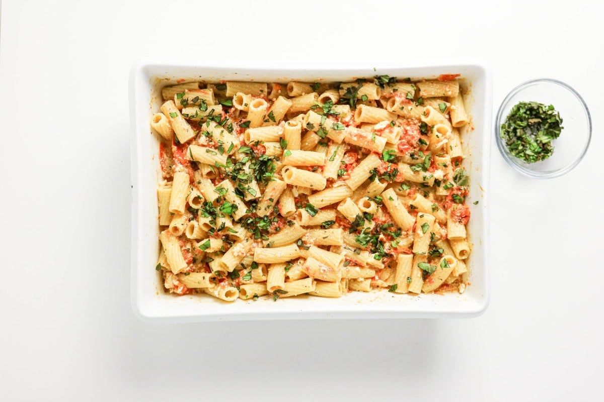Baked rigatoni pasta in a white dish, garnished with chopped herbs.