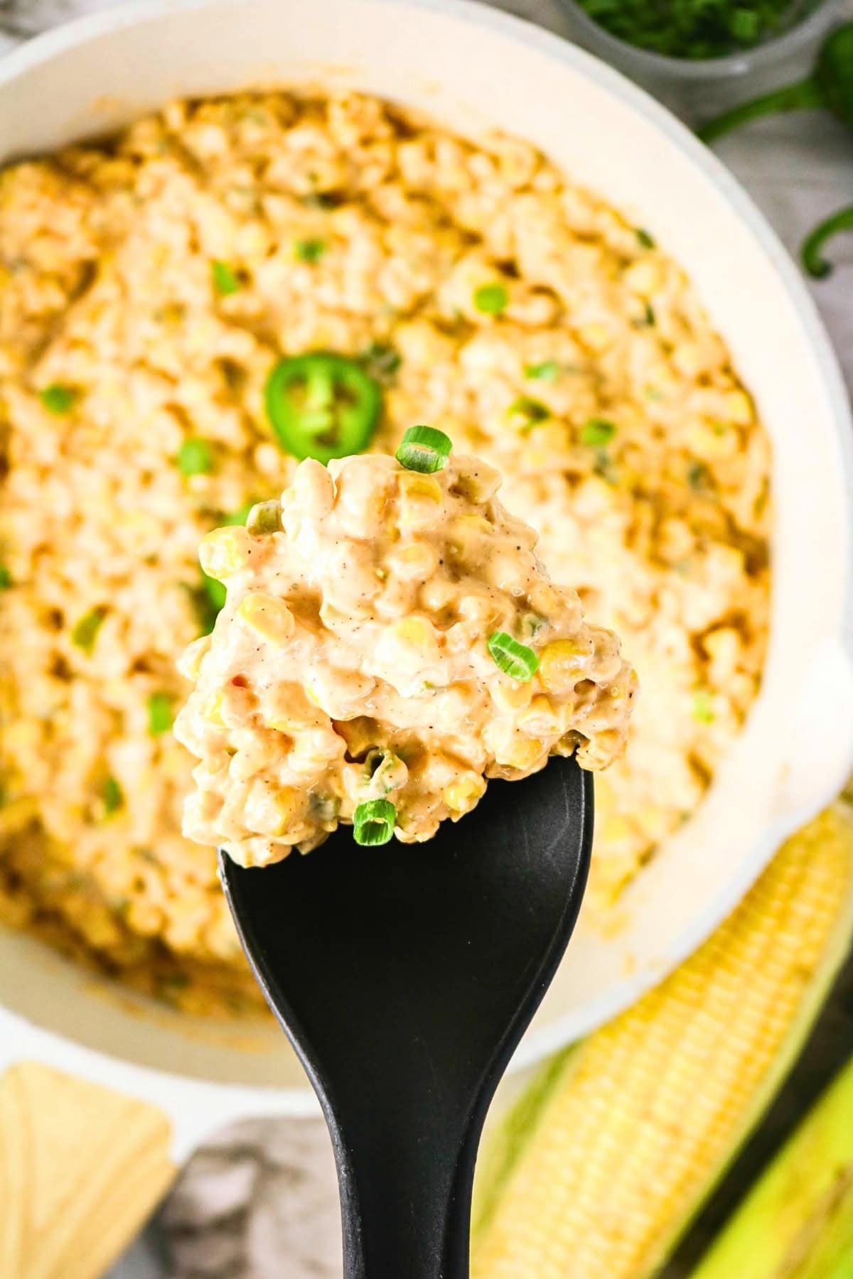Creamy corn dip with green onions on a black spoon above a bowl.
