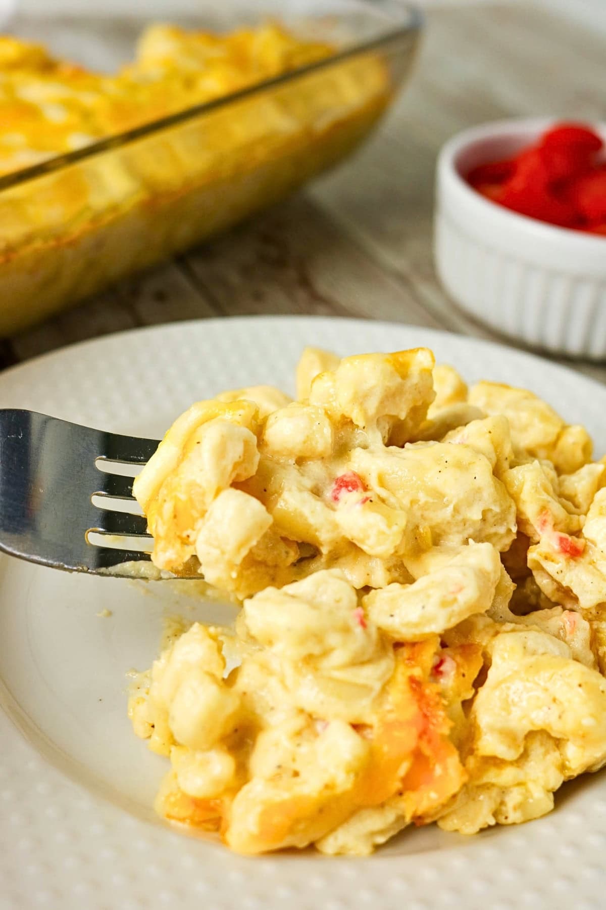 A fork holds a bite of cheesy macaroni on a white plate.