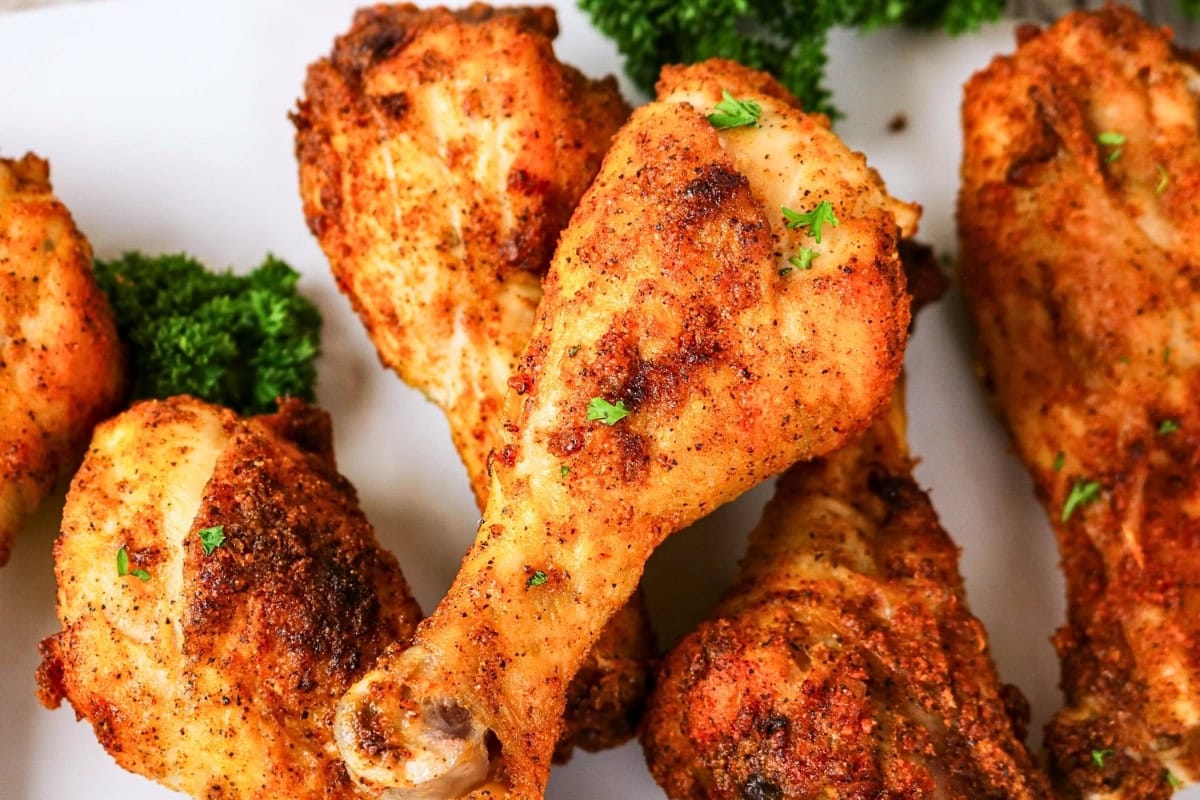 Seasoned baked chicken drumsticks with fresh parsley on a white plate.