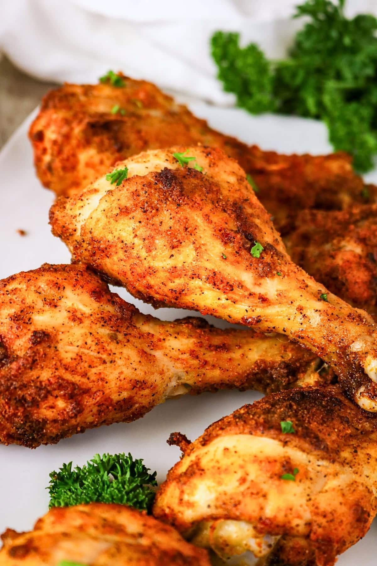 Seasoned baked chicken drumsticks garnished with parsley on a white plate.