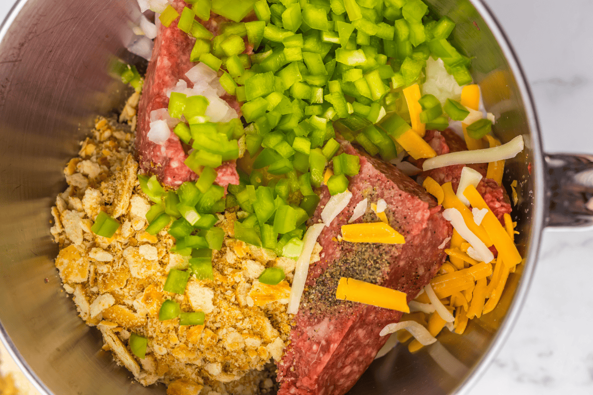Ground beef, onions, peppers, cheese, spices, and cracker crumbs in mixing bowl.