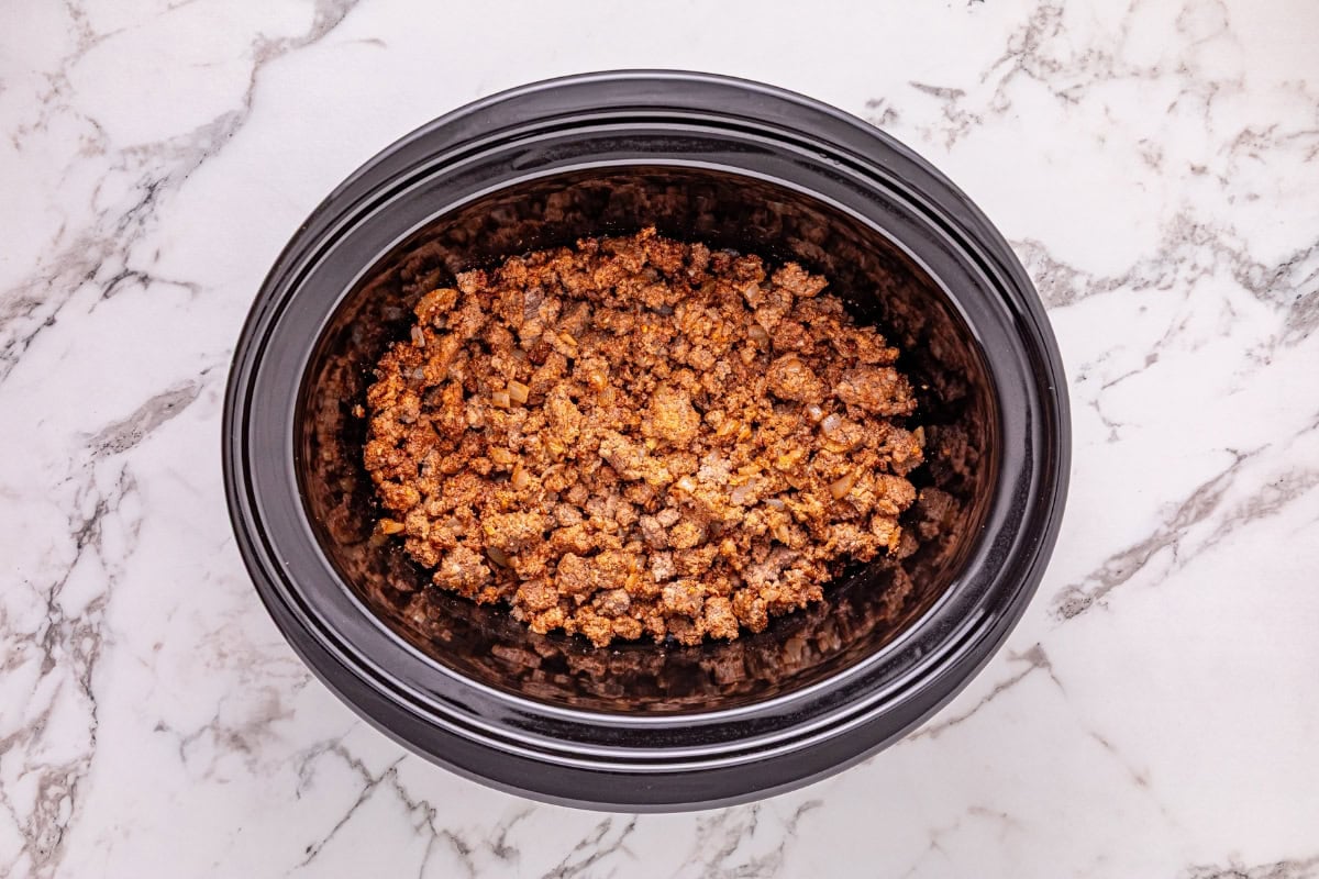 Ground meat cooked in a slow cooker on a white marble countertop.