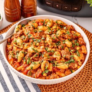 Pasta with tomato sauce, ground meat, corn, and herbs in a white bowl.