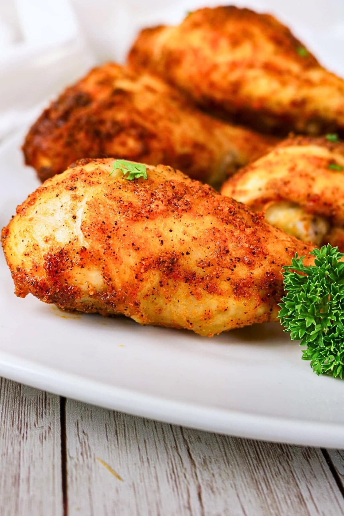 Seasoned baked chicken drumsticks on a white plate with parsley garnish.