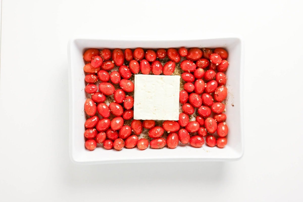 Block of feta surrounded by cherry tomatoes in a white baking dish.