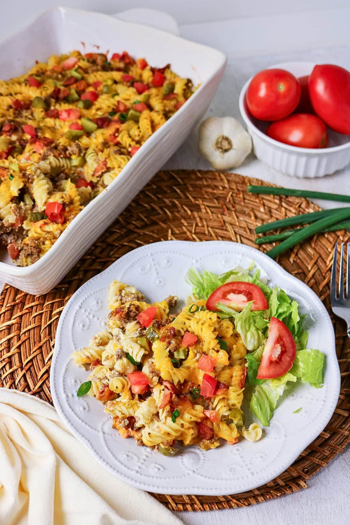 A plate of cheesy pasta bake with lettuce and tomato salad on the side.