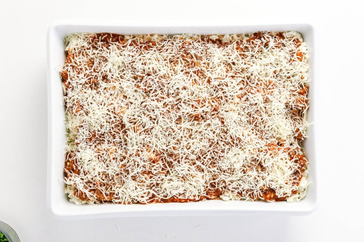 Rectangular dish with lasagna topped with shredded cheese, ready to bake.