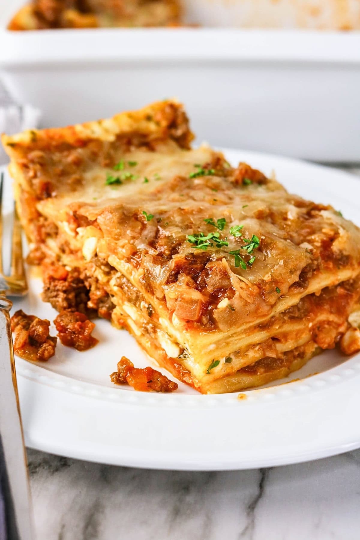 A slice of lasagna topped with parsley on a white plate.