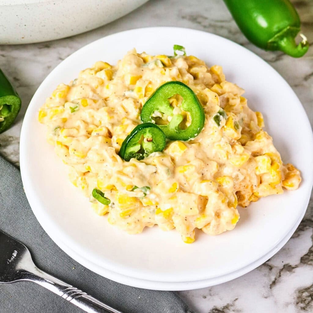 Creamy corn salad topped with sliced jalape&ntilde;os on a white plate.