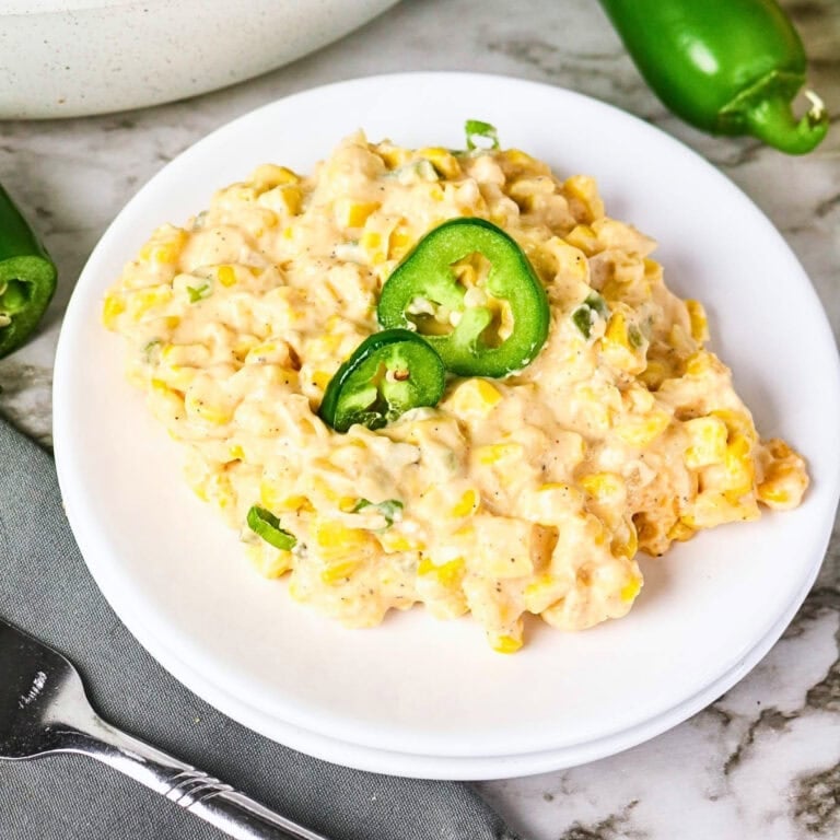 Creamy corn salad topped with sliced jalapeños on a white plate.