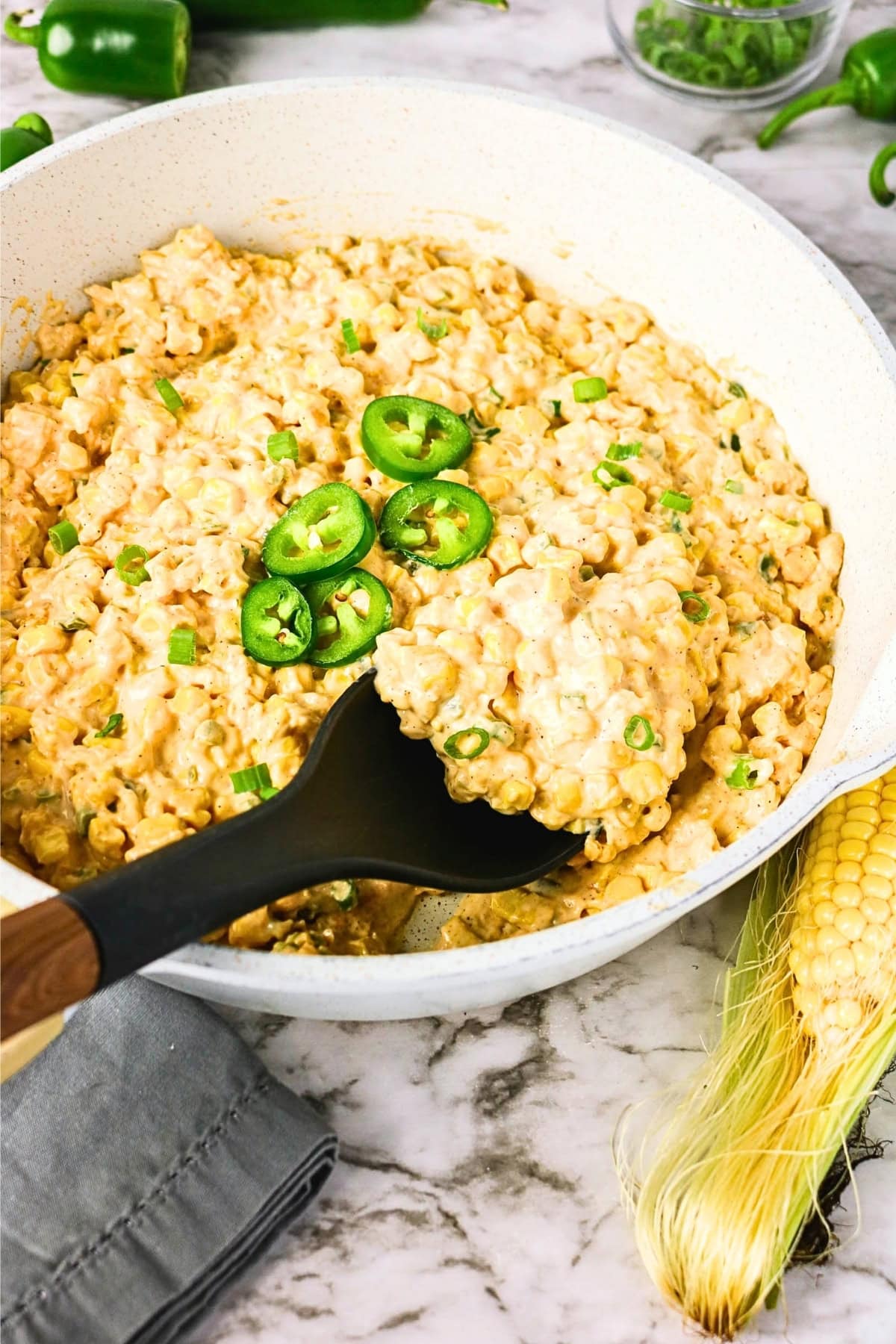 Creamy corn dish topped with sliced jalape&ntilde;os and green onions in a white pan.