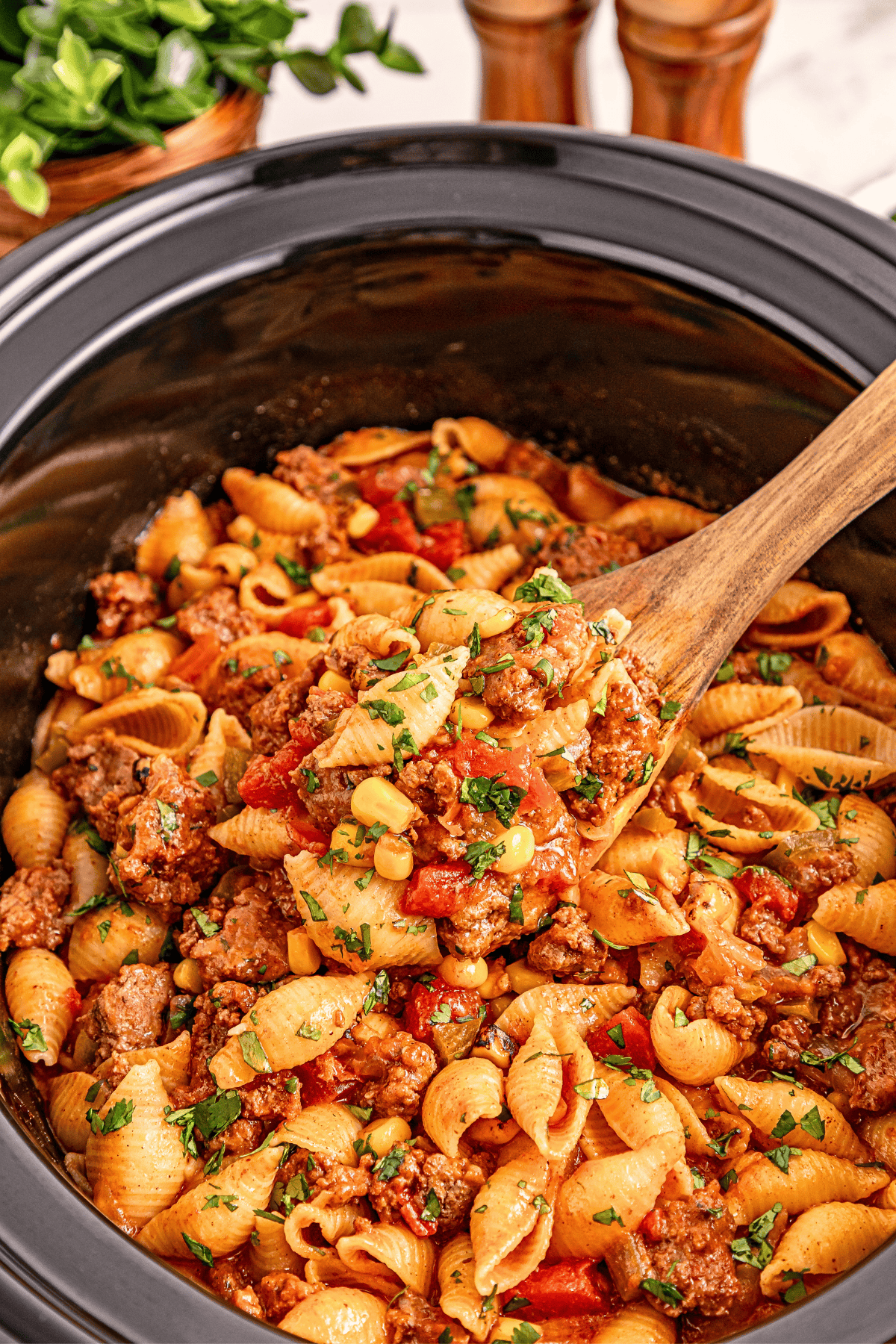 Crockpot taco pasta: shells, beef, corn, tomatoes, spices, and garnish.