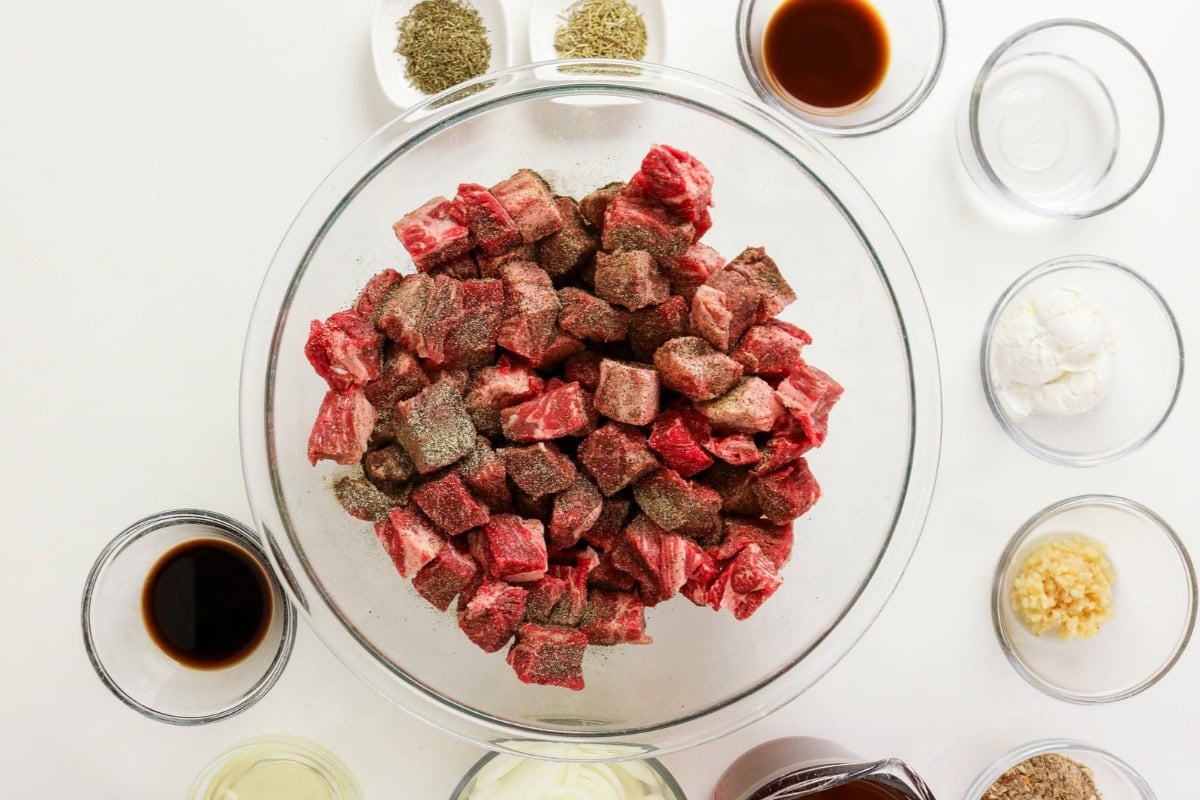 Cubed beef with pepper in bowl, surrounded by seasonings and sauces in bowls.