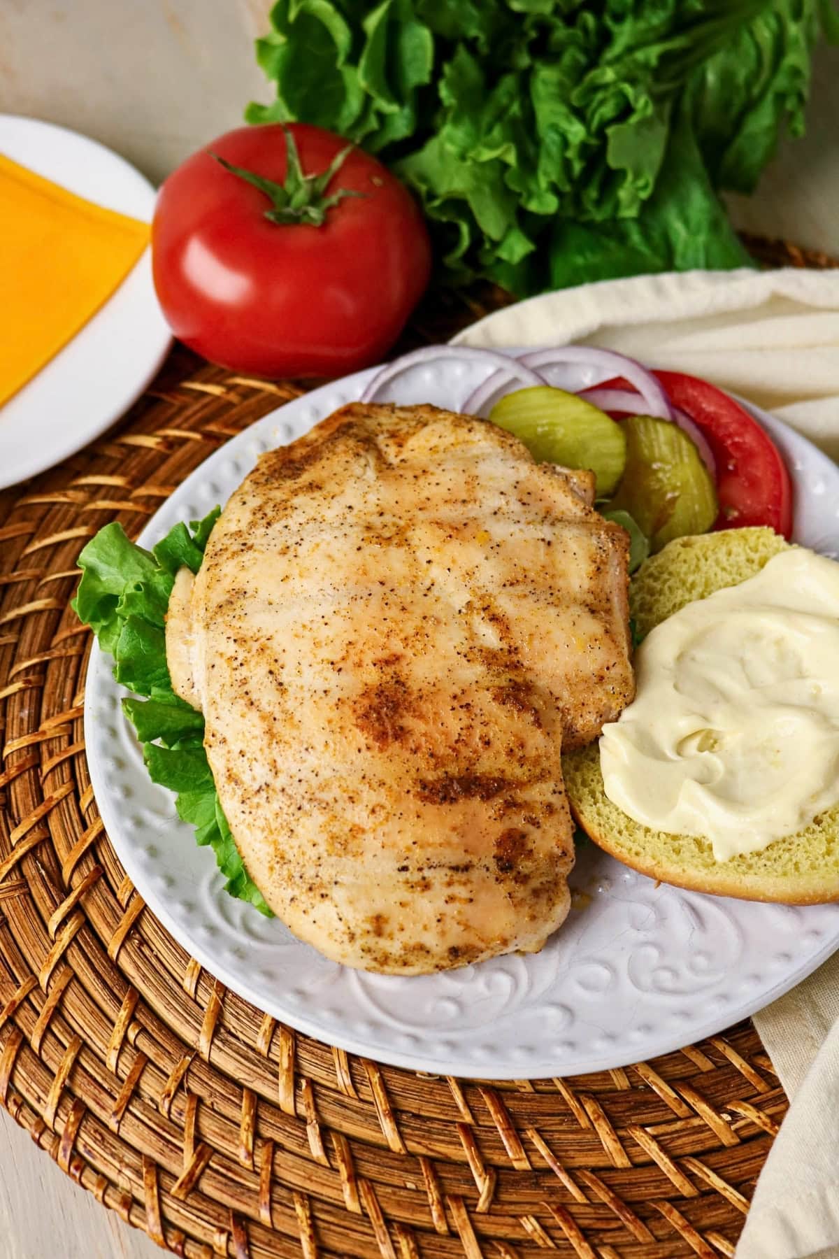 Chicken sandwich with lettuce, tomato, pickles, and mayo on a white plate.