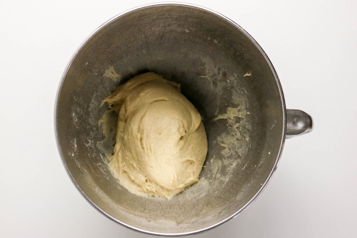 A metal mixing bowl with a ball of dough inside, on a white surface.