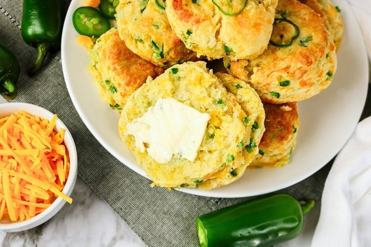 Plate of jalapeño cheddar biscuits with butter and sliced jalapeños nearby.