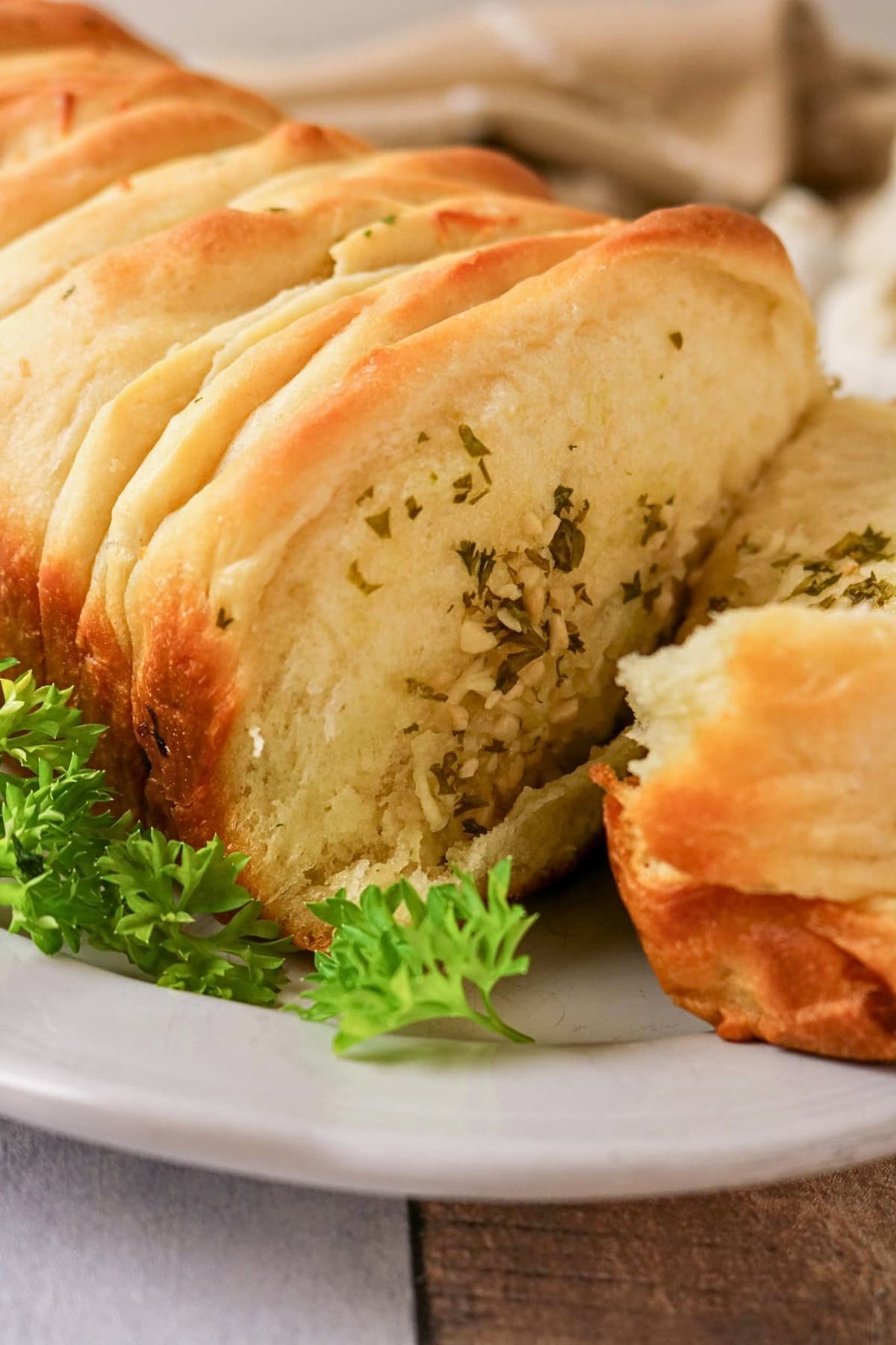 Sliced garlic herb bread on a white plate, garnished with fresh parsley.
