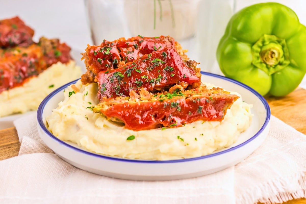Glazed meatloaf on mashed potatoes, garnished with herbs.