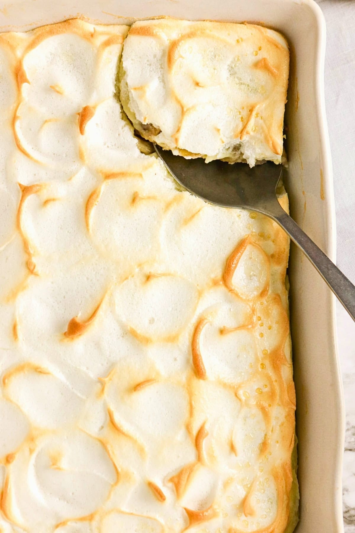 A baked dish with golden meringue topping and a serving spoon removing a piece.