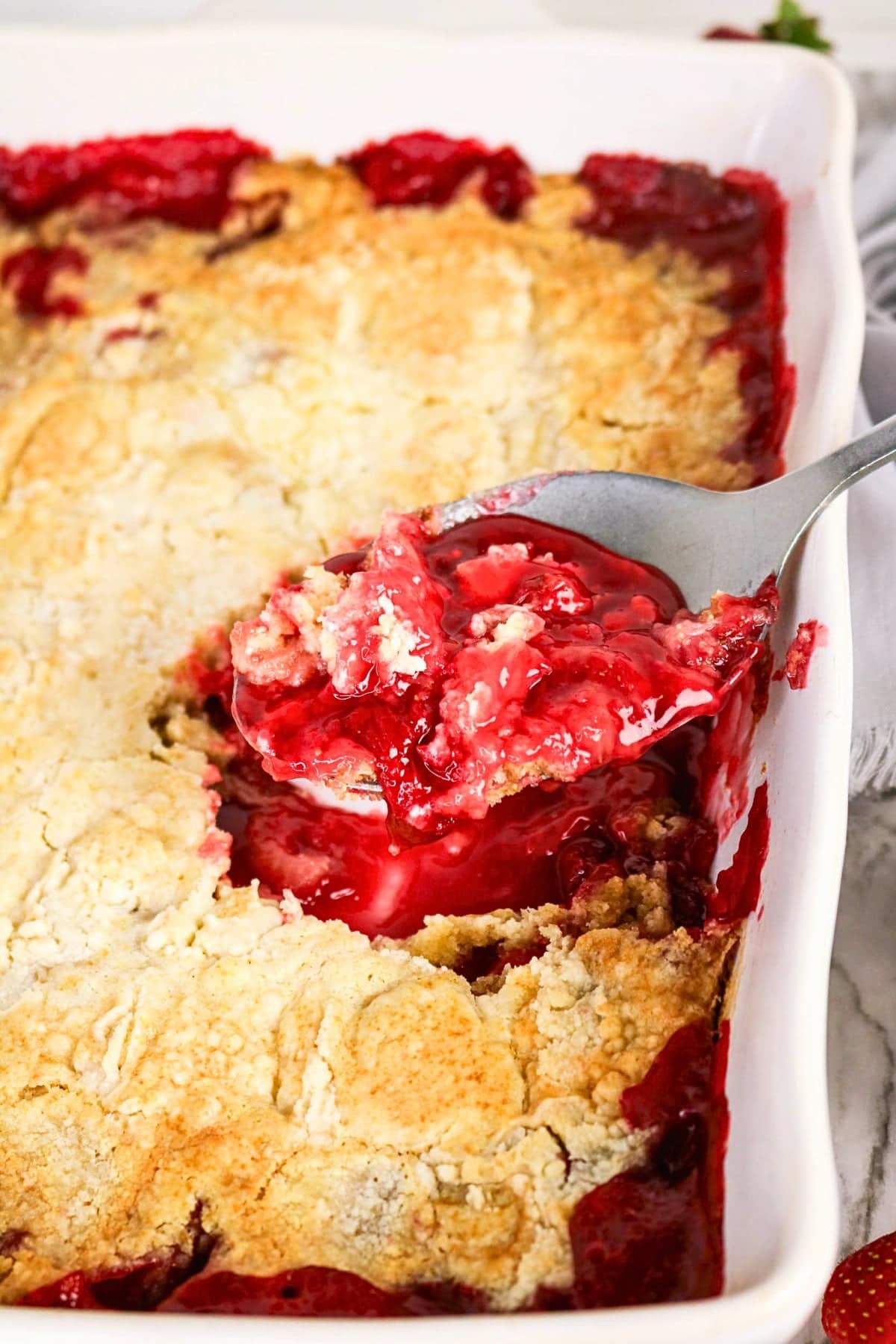 A spoon scoops berry cobbler from a baking dish with golden crust.