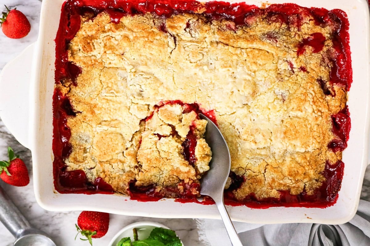Strawberry cobbler with golden, crumbly topping in a white baking dish.
