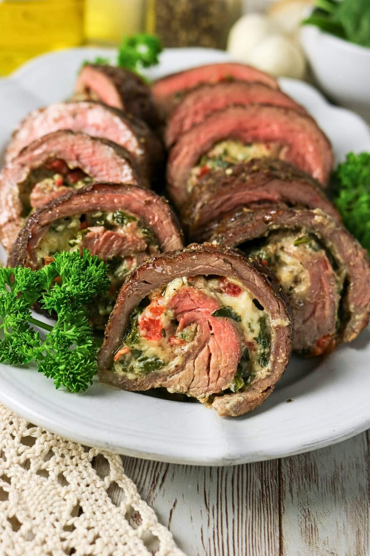 Sliced stuffed steak rolls with herbs and creamy filling on a white plate.
