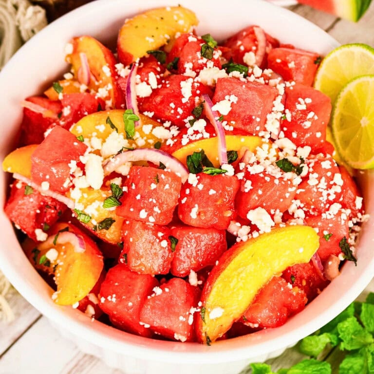 Watermelon salad with peaches, feta, red onion, herbs, and lime in a bowl.