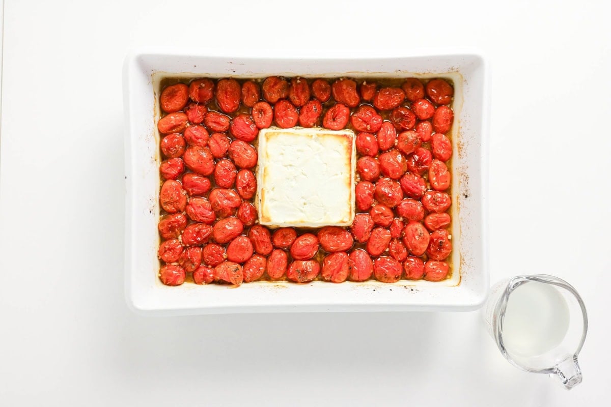 Baked feta and cherry tomatoes in a white dish, with a cup of milk nearby.