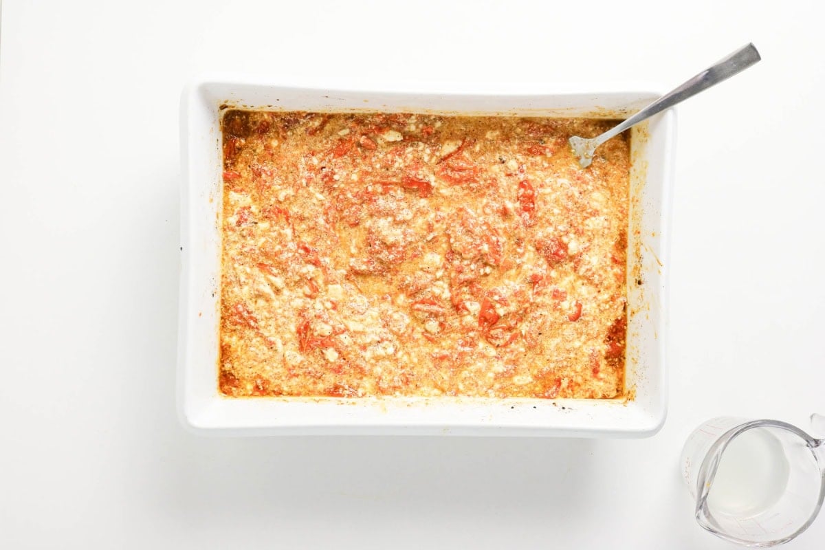 Rectangular baking dish with a cheesy, tomato casserole and a spoon inside.