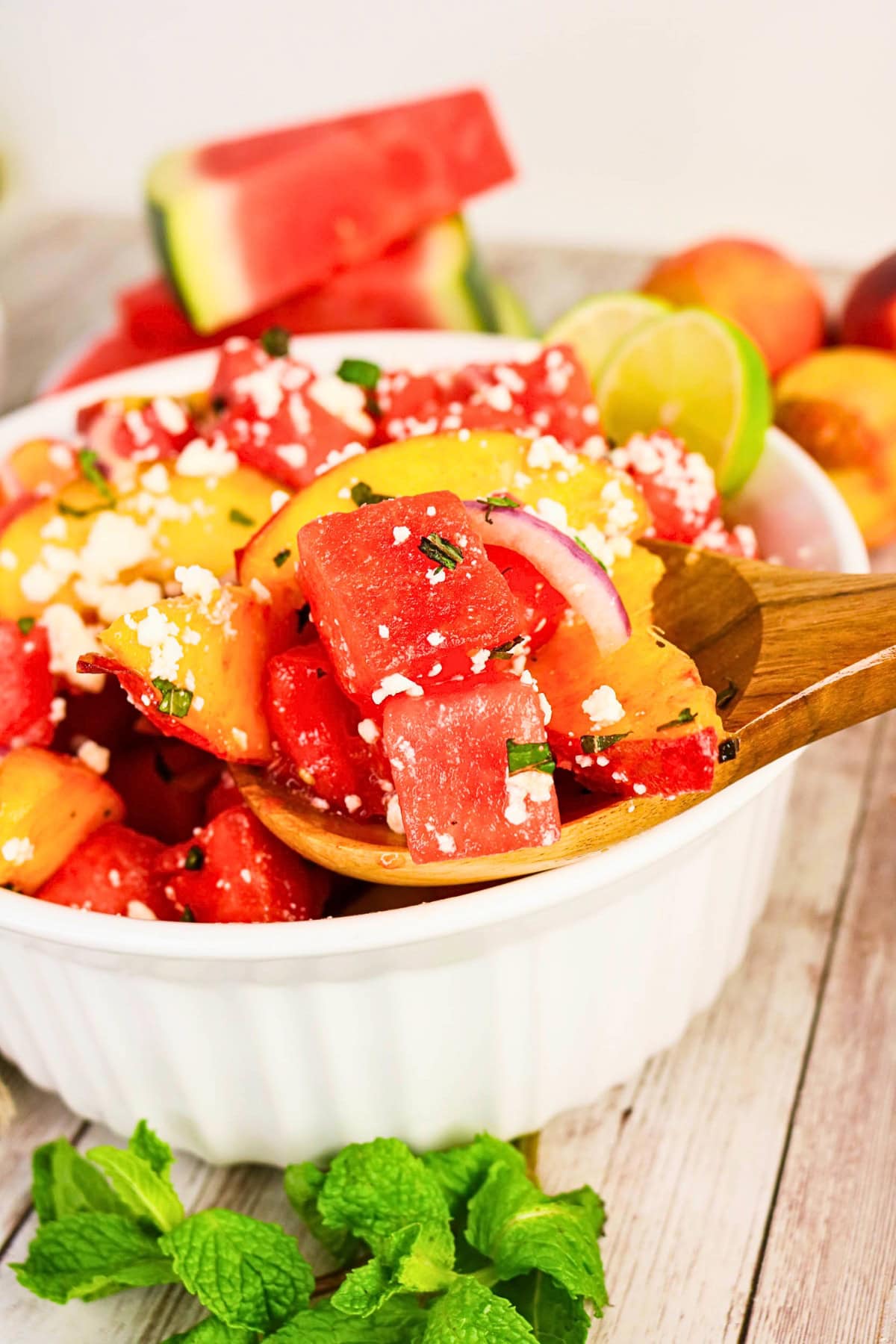 Watermelon and peach salad with feta, red onion, lime, and mint in a white bowl.
