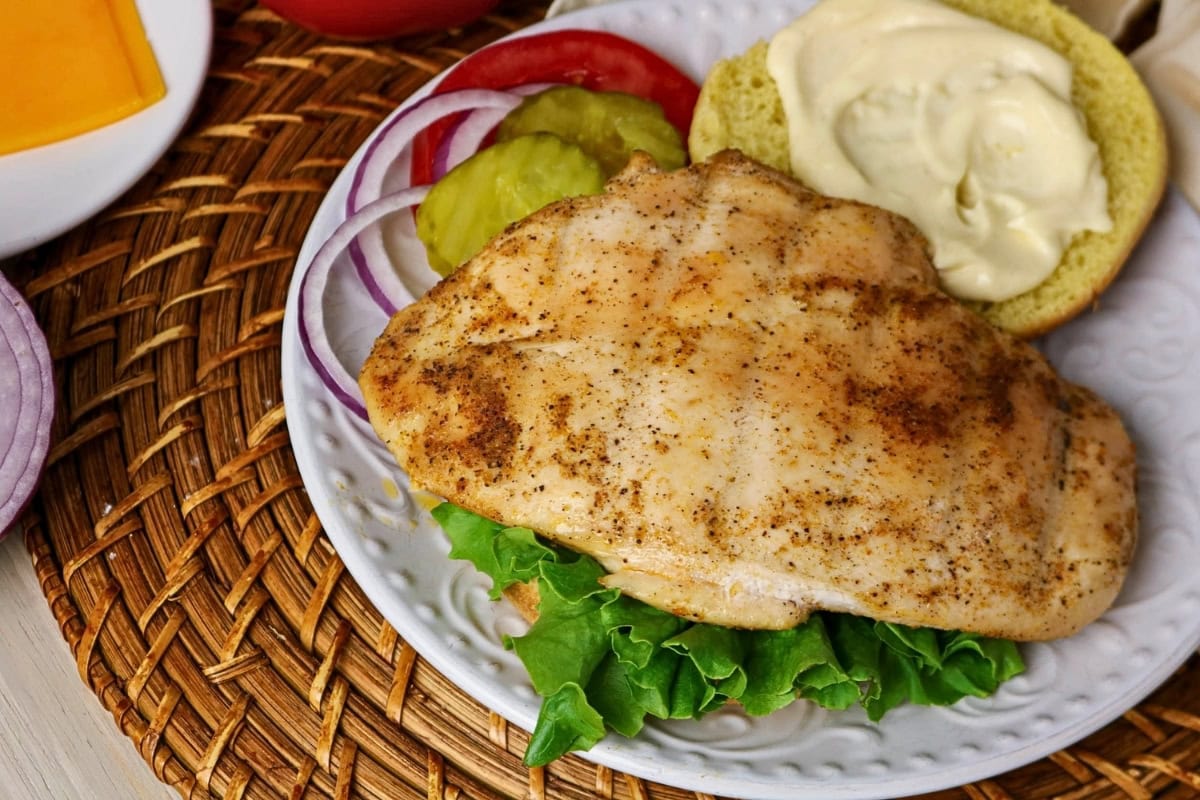 Grilled chicken breast on lettuce with onions, pickles, tomato, and a bun.